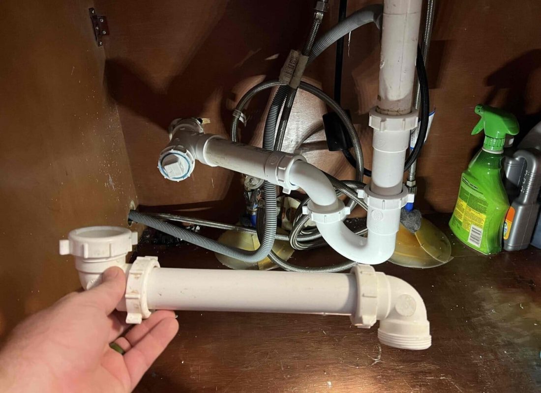 Pink Duck Plumbing technician repairing a leaking pipe in a busy Bristol, TN family home kitchen